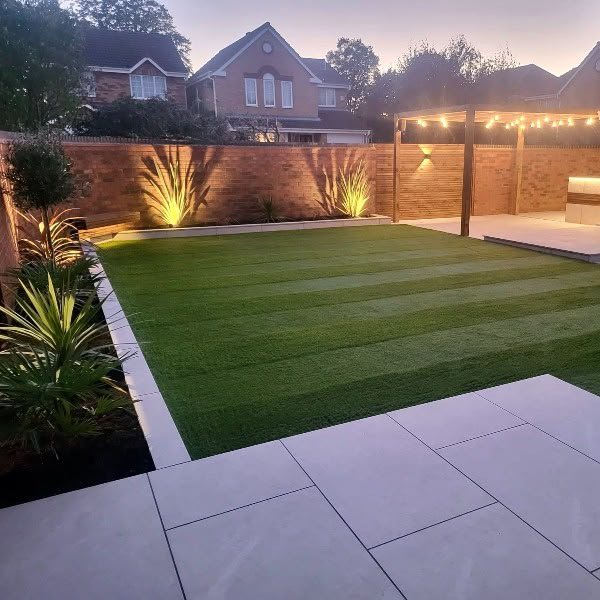 Striped artificial lawn and porcelain patio lit up at dusk