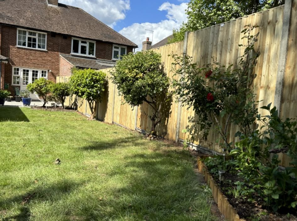 New closeboard fence behind a planted border and lawn, house in the background